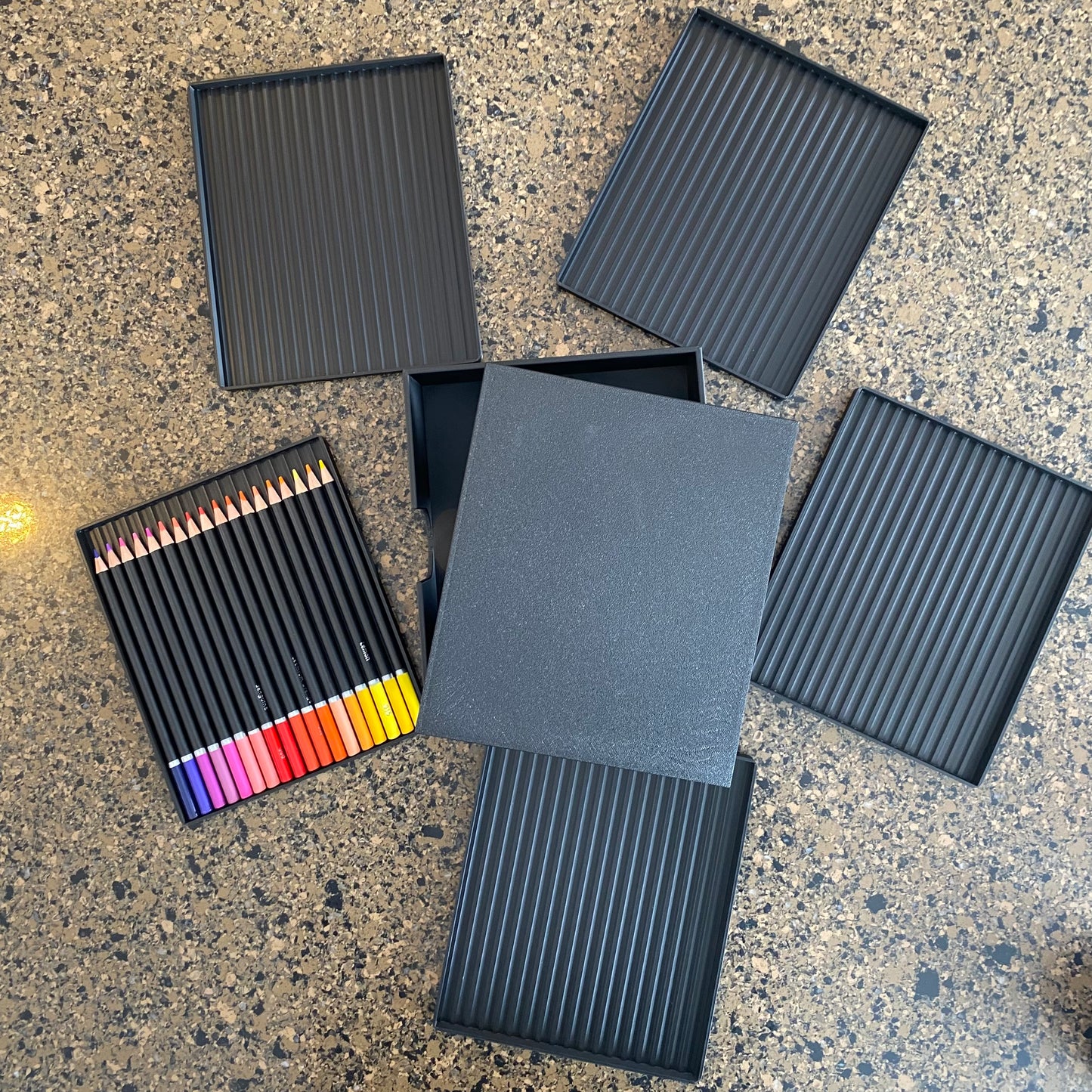 A black colored pencil caddy with multiple colored pencils visible, placed next to a gray lid or cover2