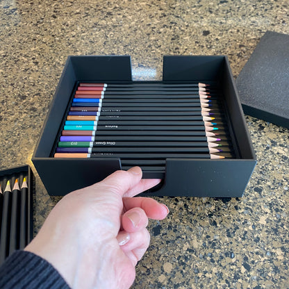A black colored pencil storage caddy open on a surface displaying multiple colored pencils inside